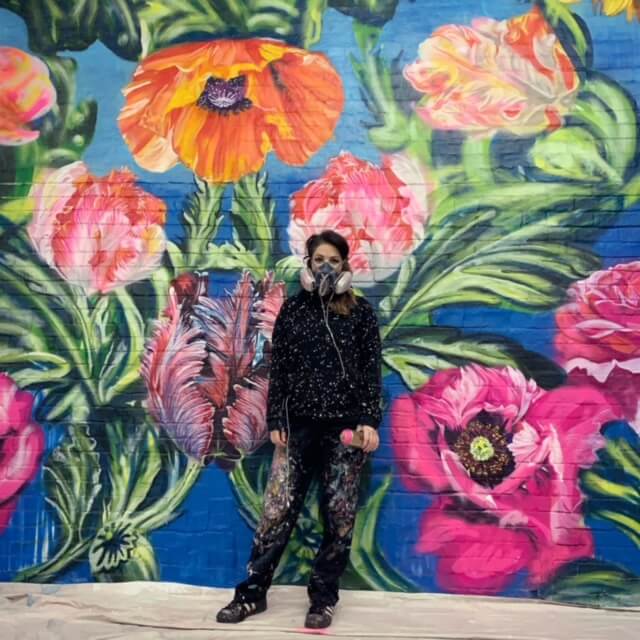 Ashley Hodder standing in front of a mural of flowers she painted