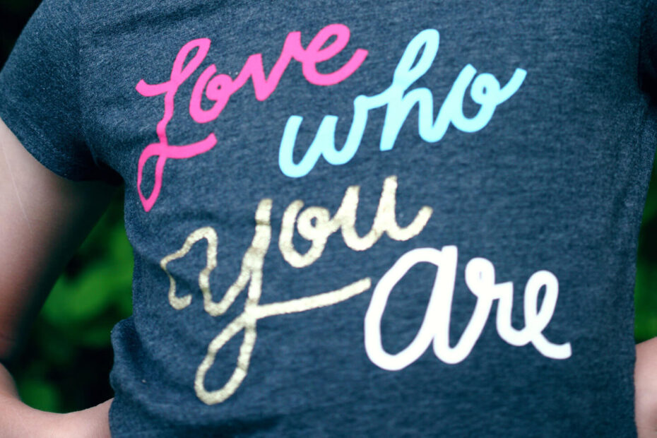 A child with facepaint standing in a heroic pose wearing a shirt that says: love who you are