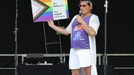 Asta Kill holding up a Lebo Pride Ally yard sign on the stage at Lebo Pride Celebration.